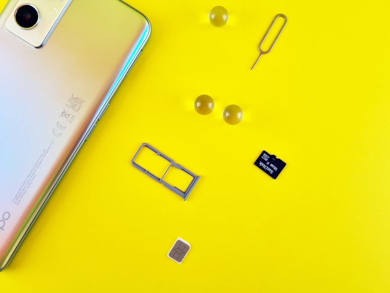 Close-up of a mobile phone with a SIM card, SIM tray, and memory card on a vibrant yellow surface.
