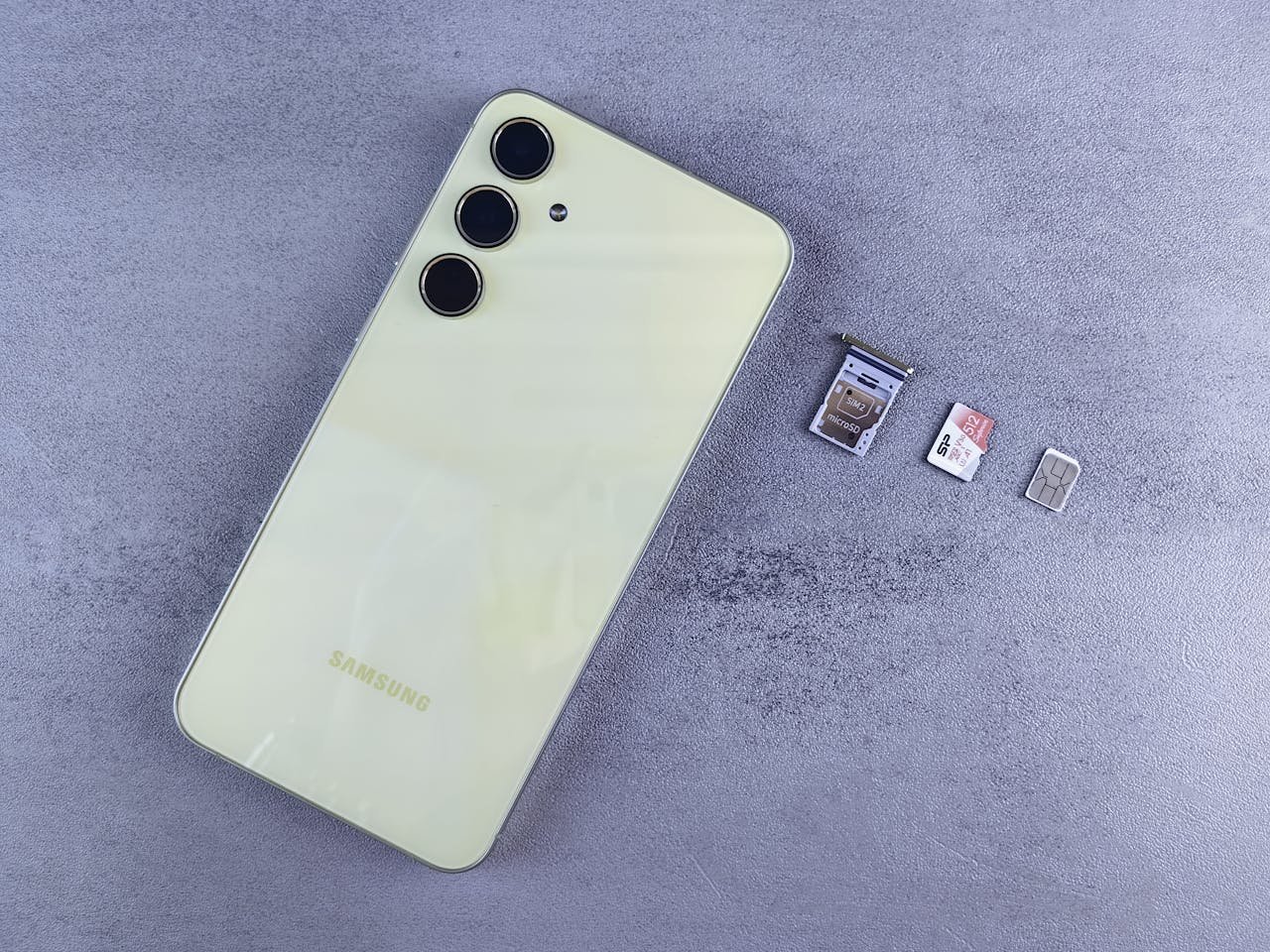 Home Yellow smartphone with SIM tray, memory card, and SIM card on gray background.