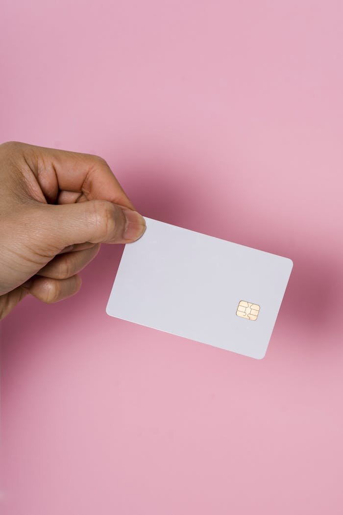 Home A hand holding a blank white SIM card on a vibrant pink background, showcasing technology.